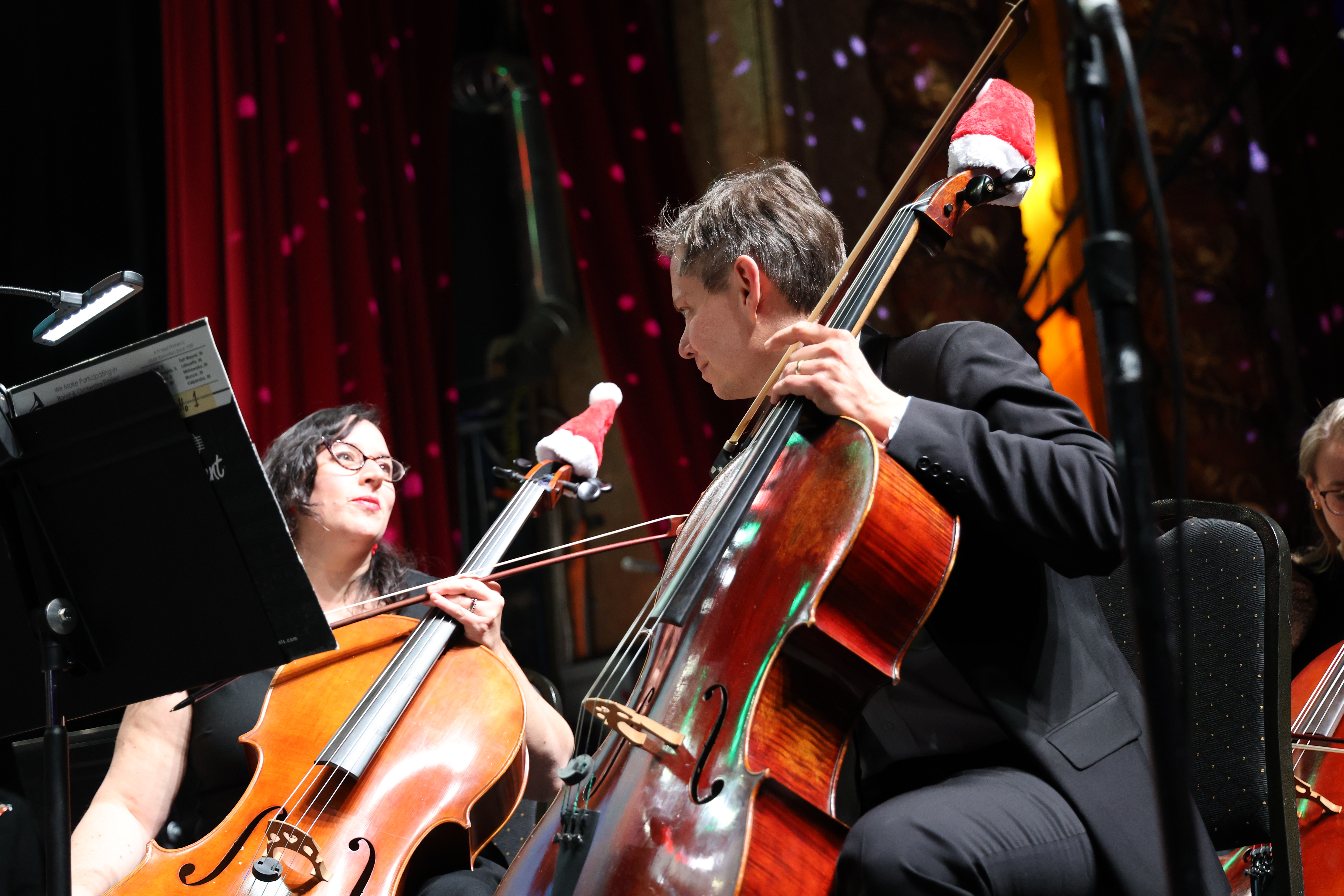 Cellists in black tie with Santa hats on instruments.